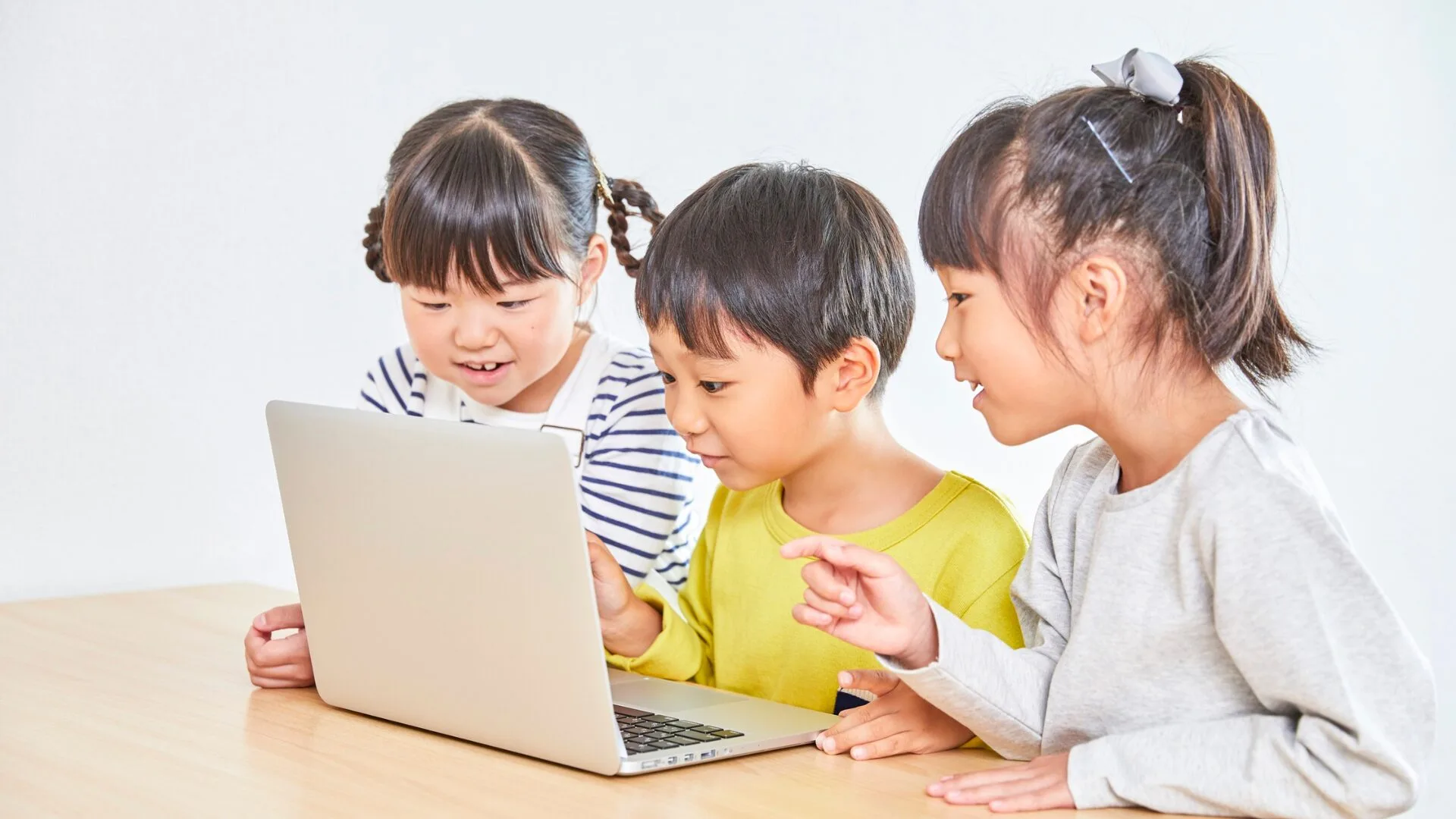 ノートパソコンの画面を一緒に覗き込む3人の子供たち