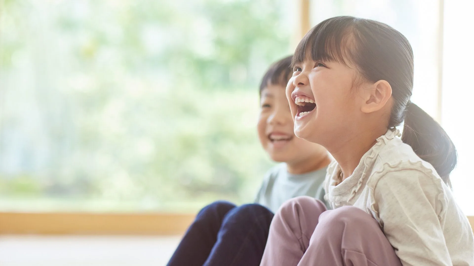 明るい部屋で、楽しそうに大笑いする小学生の女の子と男の子